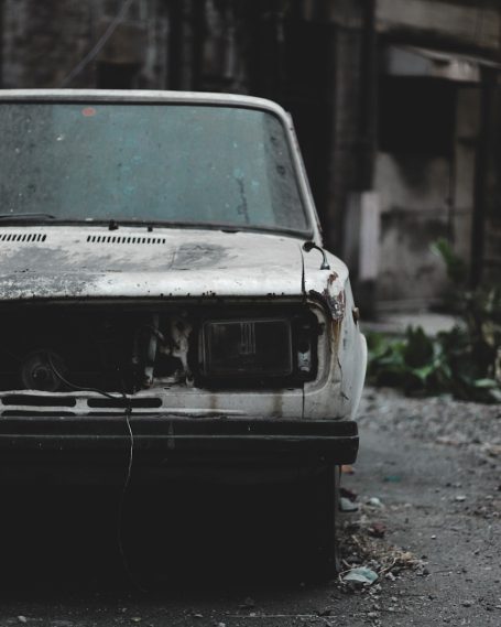 Verrostetes, beschädigtes Auto steht in einer verwilderten Umgebung.