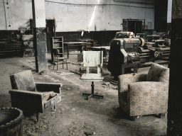 Zwei abgenutzte Stühle und ein Tisch in einer verlassenen, industriellen Umgebung.